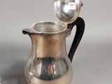 a silver pitcher with a spoon sitting next to it