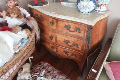 une petite poupée assise sur une chaise à côté d'une commode