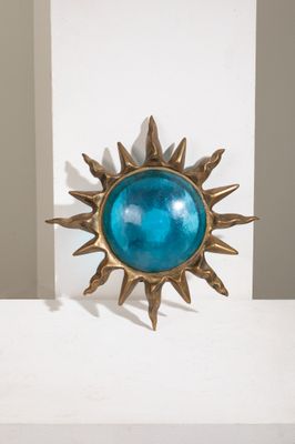 un soleil en laiton avec un verre bleu au centre, posé sur une étagère blanche