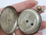 someone is holding a silver pocket watch in their hand on a white surface