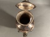 a silver tea pot and a silver cup on a table