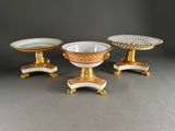 three pieces of gold and white porcelain on pedestals on a gray surface