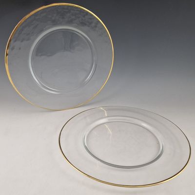 Deux assiettes transparentes aux bords dorés sont posées sur une surface blanche.