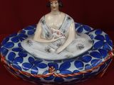 une figurine représentant une femme assise sur une assiette bleue et blanche