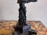 statue d'une femme tenant un oiseau, posée sur un socle posé sur une table en marbre
