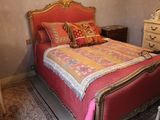 a bed with a red and gold bed spread and pillows on it