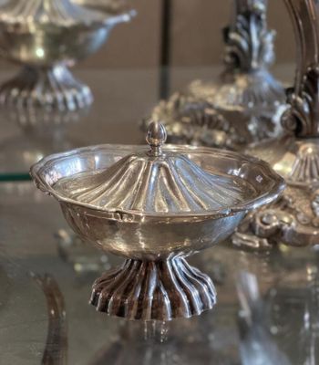 a glass table topped with silver vases on top of a glass table