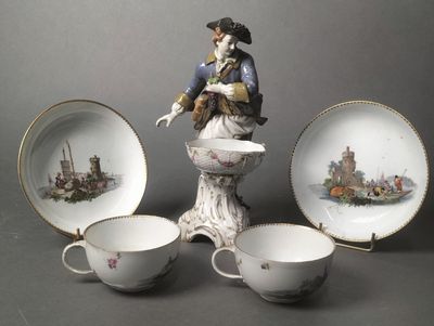 a figurine of a man on a pedestal next to three cups and saucers