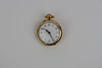 une petite montre de poche en or posée sur une surface blanche