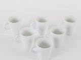 six white coffee mugs are arranged in a circle on a white surface