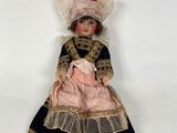 two dolls are sitting on a white surface one is wearing a pink dress and the other is wearing a black and gold dress