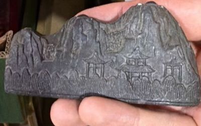 Une personne tient un objet en pierre dans la main, avec une montagne en arrière-plan.