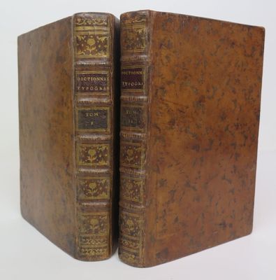 two old books are sitting side by side on a white surface
