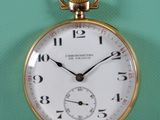 une montre de poche en or posée sur une table, avec un mur vert en arrière-plan