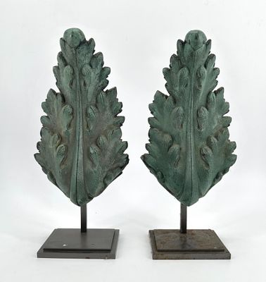 two green sculptures of leaves on stands on a white surface