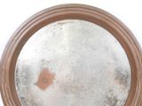 a round mirror with a brown rim on a white wall