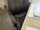 a black office chair sitting next to a desk with papers on it