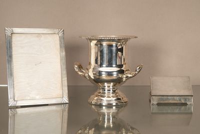un vase en argent posé sur une table en verre, à côté d'un cadre photo