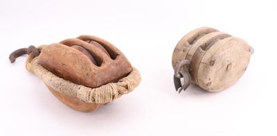 deux objets en bois posés sur une surface blanche : l'un est une poulie et l'autre est une poulie