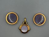 trois bijoux sont exposés sur un support gris