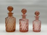 three pink glass bottles sitting next to each other on a white surface