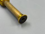 une vieille pipe en laiton avec un embout noir posée sur une surface blanche