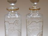 une paire de bouteilles en verre transparent rehaussées de touches dorées sur un fond blanc