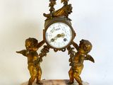 a small clock with angels on it on a marble base