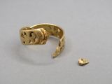 un gros plan d'une bague en or posée sur une table, à côté d'un morceau d'or