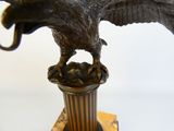 statue en bronze représentant un aigle sur un socle, avec un oiseau perché sur sa tête