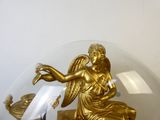 une statue en or représentant un ange tenant un poisson, placée sous un dôme en verre