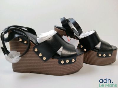 une paire de sandales à talons compensés noires et marron posées sur une surface blanche