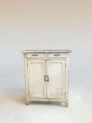 une petite armoire blanche à deux portes, avec un tiroir en dessous