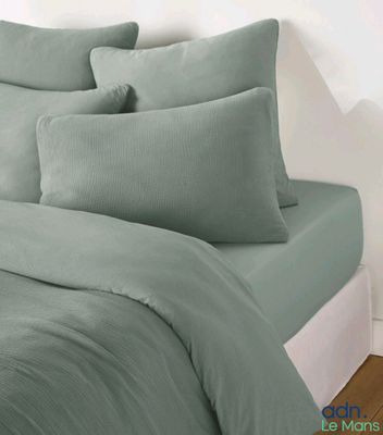 une photo d'un lit avec une couette et des oreillers verts