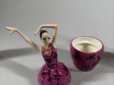 a figurine of a woman in a pink dress next to a cup