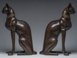 two bronze statues of cats sitting on their hind legs, one with a collar around its neck and the other with a collar around its neck