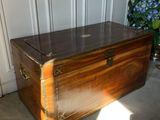 a wooden trunk sitting on the floor next to a vase of flowers