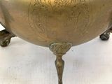 un bol ancien en laiton muni d'une anse, posé sur une surface blanche