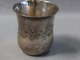 an old silver cup sitting on top of a table next to another cup