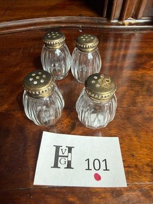 quatre salières et poivrières en verre posées sur une table, avec une étiquette de prix