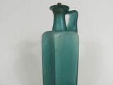 a green glass vase with a gold handle on a white surface