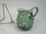 a small green vase with flowers and butterflies on it next to a gold triangle