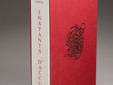 un livre rouge posé sur une table blanche, près d'un mur gris