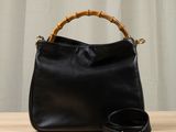 a black leather bag with bamboo handles and a belt on a wooden table