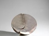 sculpture en argent représentant un objet circulaire posé sur une surface blanche