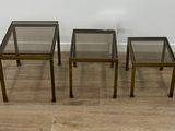 trois tables d'appoint en verre et en laiton posées sur un parquet