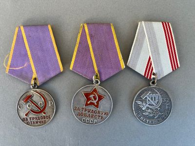 three medals are displayed on a gray surface with a red star and hammer