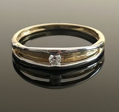 un gros plan d'une bague en or et en argent posée sur une surface noire