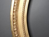 a close up of a gold oval mirror on a black wall