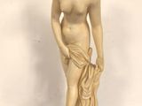une statue blanche représentant une femme tenant une fleur, posée sur un fond bleu